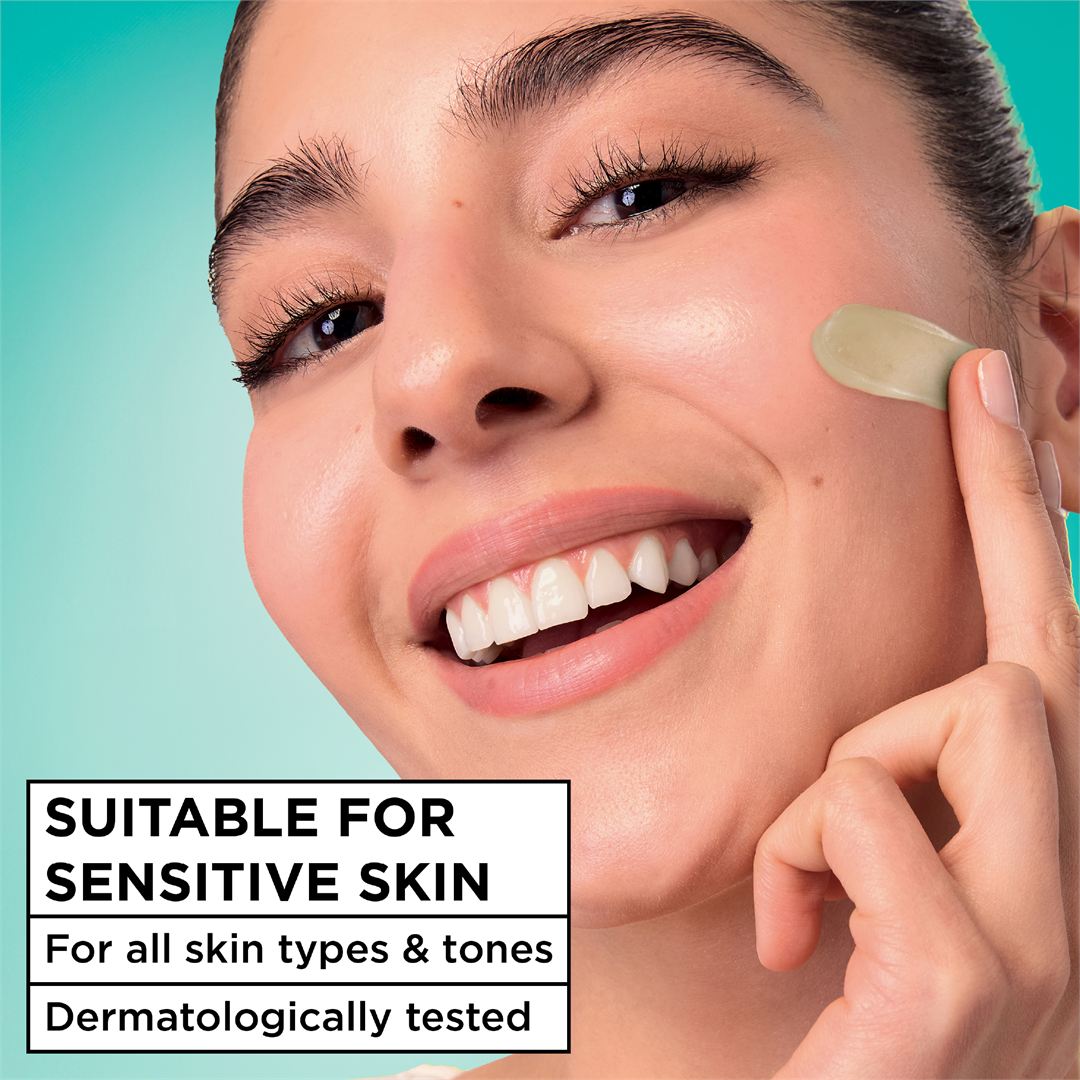 Close-up of a smiling woman applying a translucent green peel-off mask to her cheek against a teal background, with text stating 'SUITABLE FOR SENSITIVE SKIN' and 'For all skin types & tones Dermatologically tested'.
