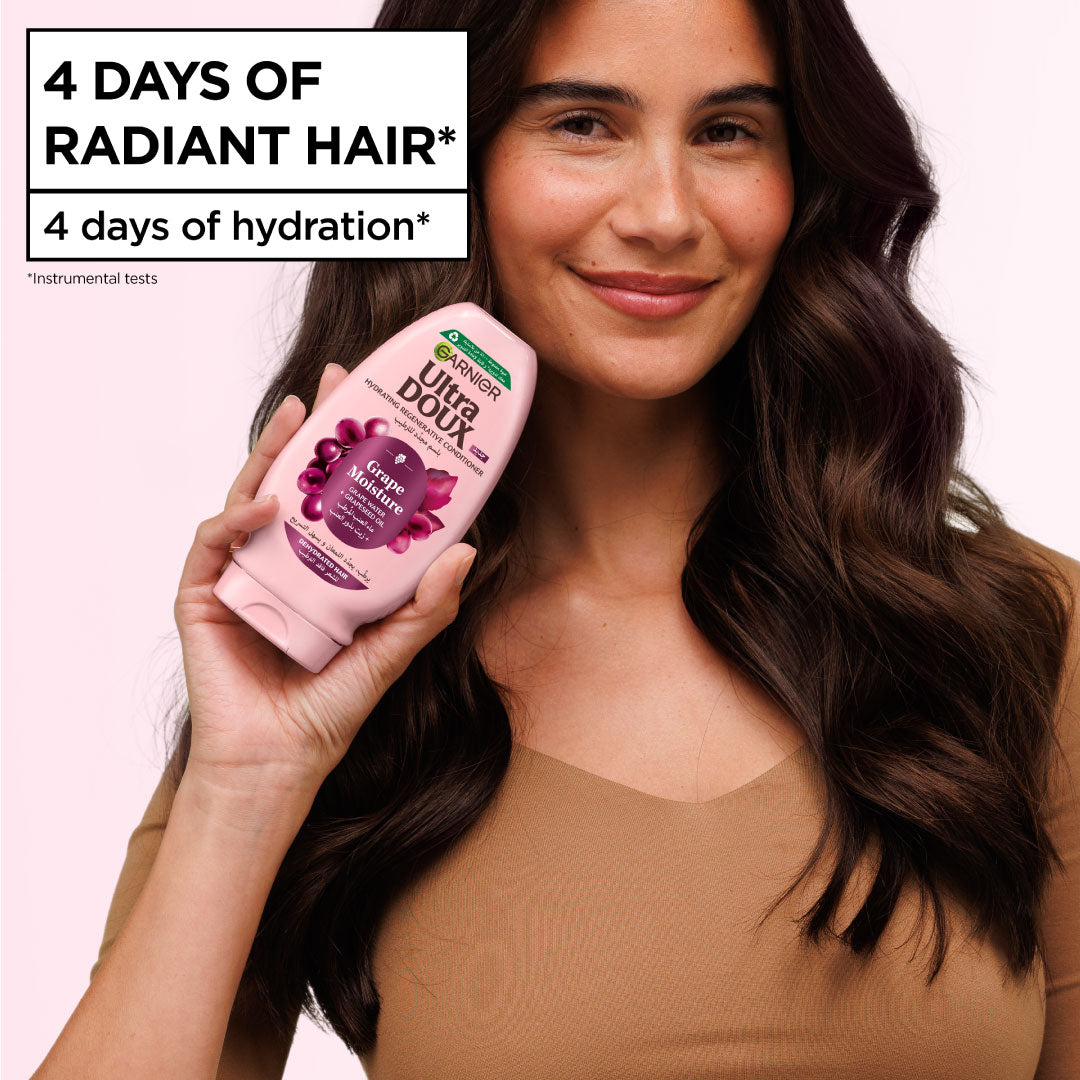 Woman holding a bottle of Ultra Doux shampoo with text about radiant hair and hydration on a pink background