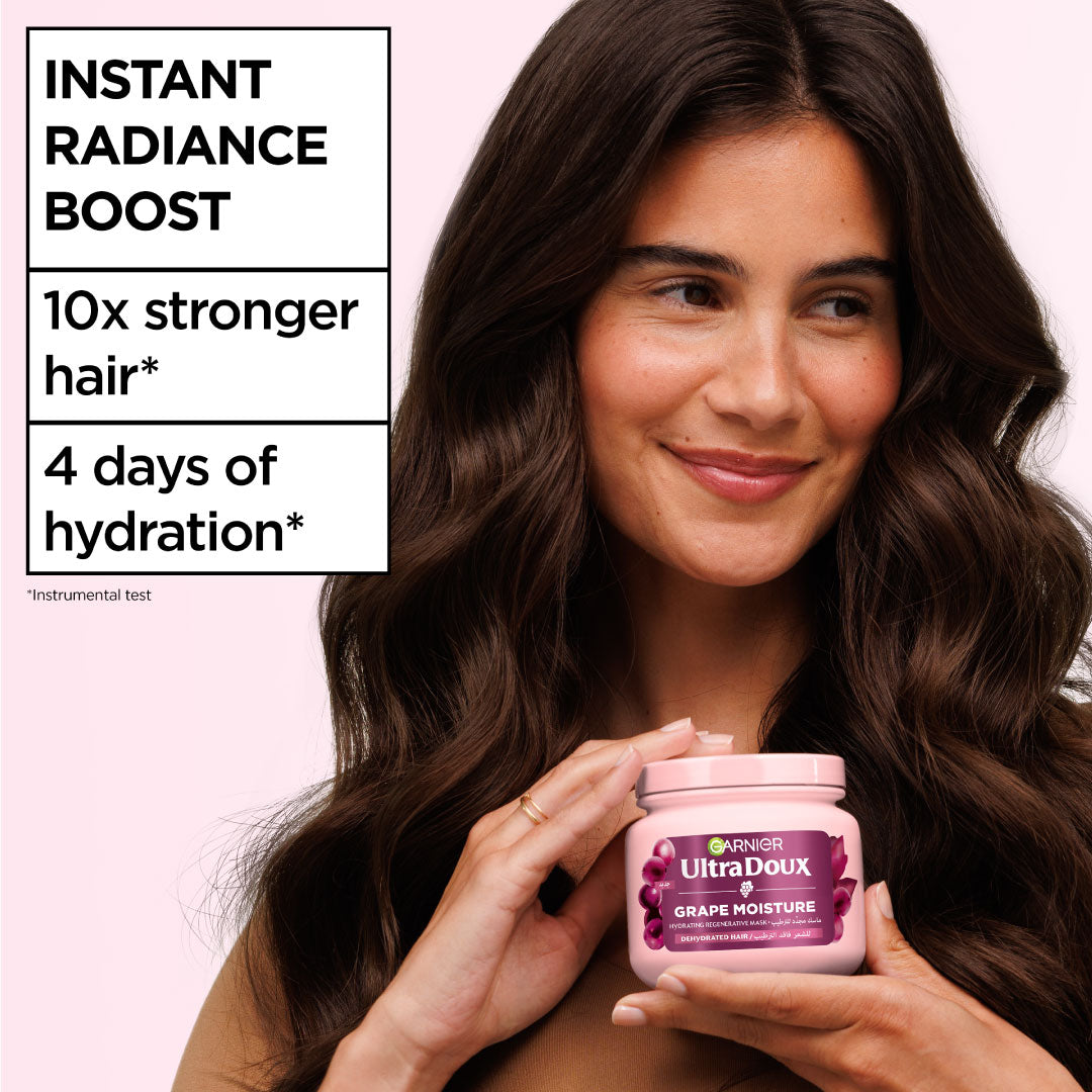 Woman holding a Garnier Ultra Doux hair care product with text about hair benefits on a pink background